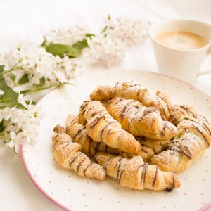 A plate of fresh croissants and a cup of coffee with blooming white flowers.