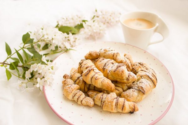 A plate of fresh croissants and a cup of coffee with blooming white flowers.
