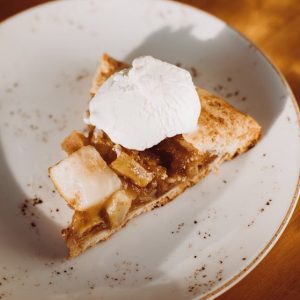 A delicious slice of apple pie topped with whipped cream on a rustic ceramic plate.