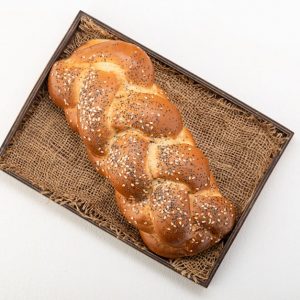 Overhead shot of a golden braided challah bread with sesame seeds, presented on a rustic woven tray.