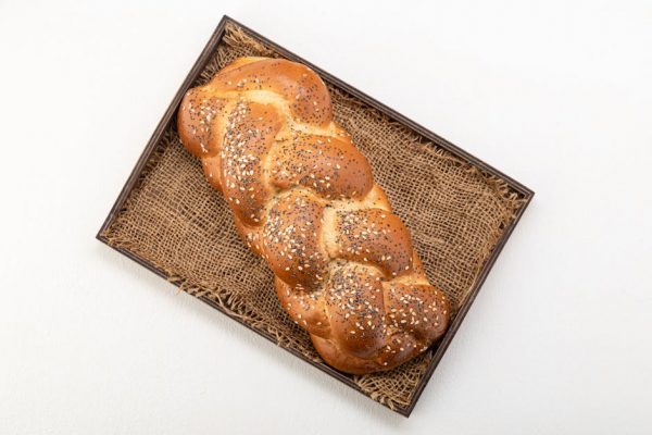 Overhead shot of a golden braided challah bread with sesame seeds, presented on a rustic woven tray.